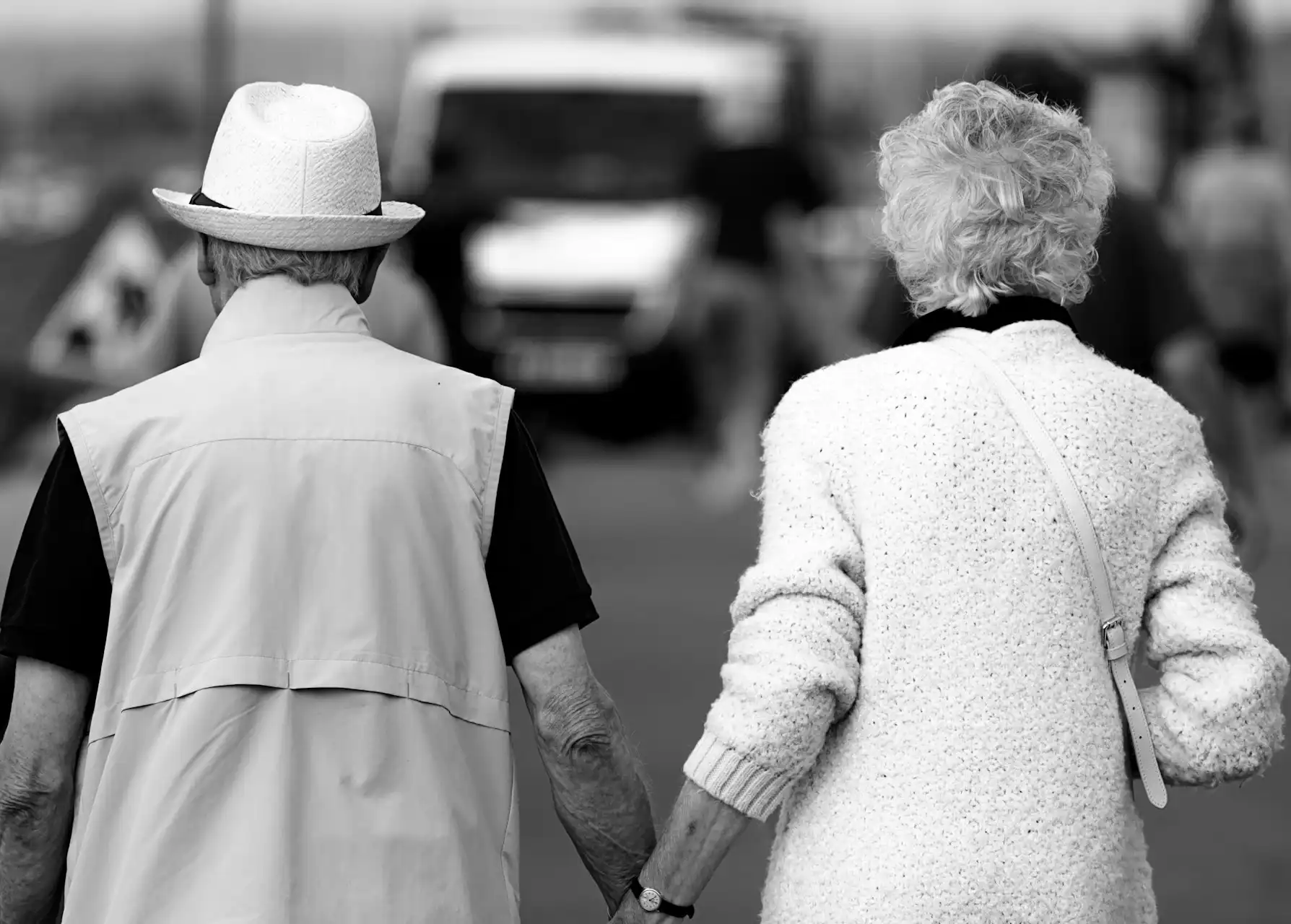 In the picture, in black and white, we can see an old couple walking hand in hand.